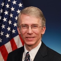 a man with glasses and the American flag in the background